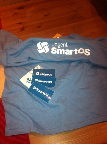 SmartOS swag on a table, include a t-shirt and some stickers.